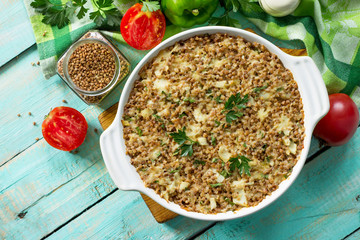 Fish casserole with buckwheat and various greens and vegetables on a kitchen wooden table. Flat lay, top view with copy space.