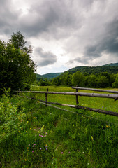 Fototapeta premium wooden fence on a rural meadow in mountains. lovely agriculture scenery on a cloudy summer day