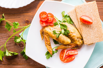 Baked chicken wings with cherry tomatoes, greens and bread on a plate. Top view