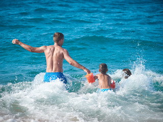 Mom father and son running into the sea water. Back view.