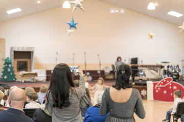 parent take photo of kid 's show on stage with smartphone at school for background usage .