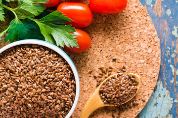 Flax seeds in a spoon and a bowl, fresh vegetables on a wooden table. Top view. Close-up