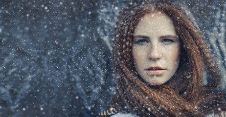 Beauty Christmas fashion model girl red hair freckles on face, portrait drops snow. portrait of a young woman in a cold winter. Stylish women's, fashionable hairstyle, make-up. advertising