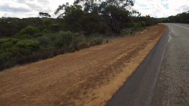 Kurvige Autofahrt im Linksverkehr auf einen Highway in West-Australien mit Kamerablickwinkel auf den linken Straßenrand