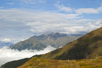 morning view from a mountain plateau to neighboring mountain ranges, towering above the clouds; near is the trail of the tourist route with a road sign..