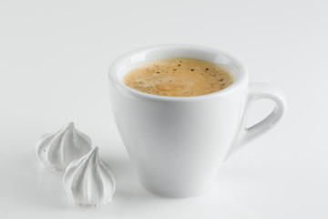 Coffee in a white porcelain cup, black coffee and white meringues on a white surface