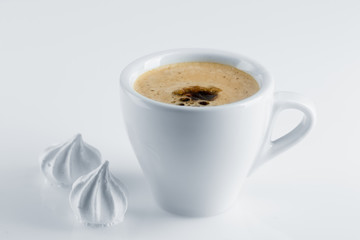 Coffee in a white porcelain cup, black coffee and white meringues on a white surface