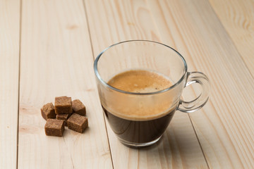 hot coffee with foam in a glass on a wooden table, brown sugar