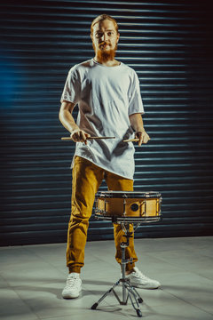 Handsome guy behind the drum kit on a dark background in t-shirt and trousers