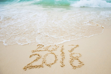 2017 is going end of year and Happy new year 2018 written on sand beach with blue wave, New Year 2018 is coming concept.