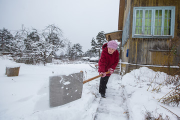 Elderly woman cleans the snow near his home in the village.