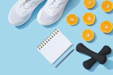 Female fitness flat lay, sneakers, dumbbells, notebook planner on blue background, healthy sports lifestyle New Year resolution