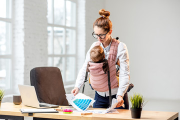 Exhausted businesswoman working with paper documents with her baby son at the office