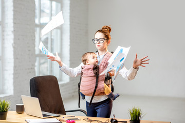 Multitasking and exhausted businesswoman throwing up a documents standing with her baby son during...