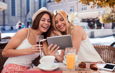 Friends meeting in a cafe. Young women drinking coffee and have fun with tablet. Consumerism, lifestyle concept
