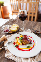 baked duck leg with berry sauce with apples on a white plate with a glass of red wine on a wooden table - 185759255