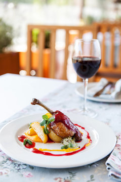 baked duck leg with berry sauce with apples on a white plate with a glass of red wine