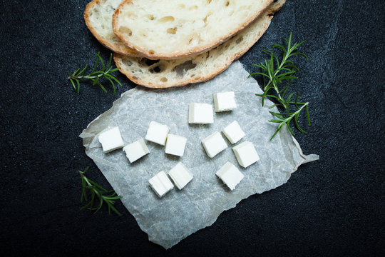 Food for a small snack, traditional feta cheese, bread and rosemary on a black background.