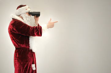 Santa claus man looking through binoculars and showing ahead isolated on gray background. Side view.