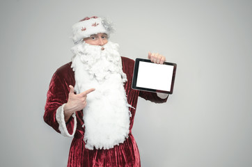 Santa Claus hold in hands a tablet computer with blank screen with copy space isolated on gray background. Christmas congratulatory message.