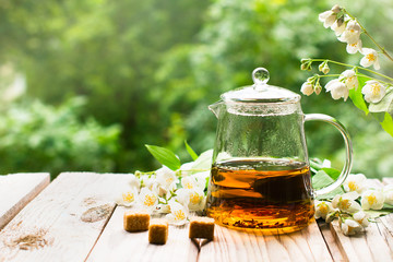 Teapot with jasmine tea and flowers on the wood background