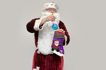 Angry bad Santa Claus pulls out a toy ball from a Christmas sock isolated on gray background.