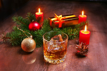 christmas decoration with glass of cognac or whiskey, red candles, gift box and christmas tree. Selective focus.