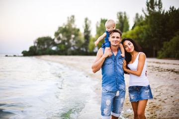 beautiful young family on vacation with baby. The father holds the blonde girl in her arms, and the brunette's mother hugs her husband. The concept of a family beach holiday summer near the sea