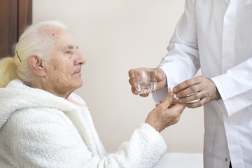 Pielęgniarz podaje szklankę wody starej kobiecie podczas podawania leków. Pielęgniarz nadzoruje branie leków przez starą kobietę.  - obrazy, fototapety, plakaty