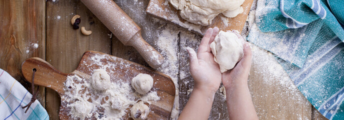 children's hands and dough with flour on a wooden table and a green towel, rolling pin and board