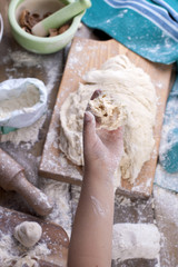 children's hands tear off the dough, the flour is scattered on a wooden table and a green towel, rolling pin and board