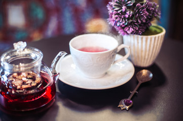 Kitchen composition of a teapot with fruit tea, elegant white cup with steam coming from it and purple oriental background