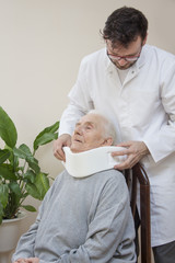 Lekarz ortopeda zakłada biały kołnierz ortopedyczny bardzo starej kobiecie siedzącej na...