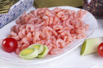small shrimps on a plate and on lasagna sheets cherry tomatoes, on a white concrete background