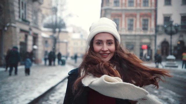 A frame behind a girl walking back is smiling walks around the city smiling charming happiness holiday lifestyle close-up snowflakes cold snow white beauty face winter slow motion