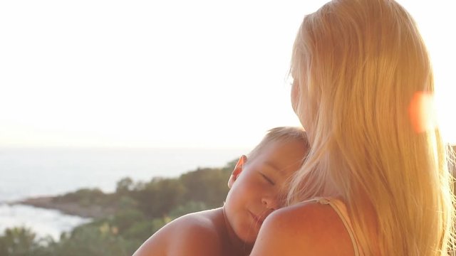 young mother lulls her son on sunset background.