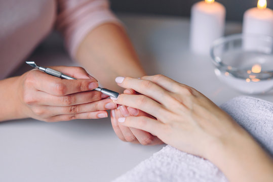 Nail care. Closeup of beautiful woman hands getting manicure in spa salon. Female manicurist cleaning cuticle with professional manicure pusher tool. Cosmetic procedure.