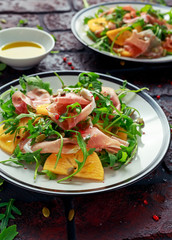 Fresh Tasty Persimmon salad with arugula, parma ham, olive oil and herbs. autumn, winter healthy food