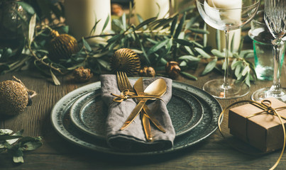 Christmas or New Years eve celebration party table setting. Plates, golden cutlery, festive branch decoration, candles and gliterring toys over wooden table background, selective focus