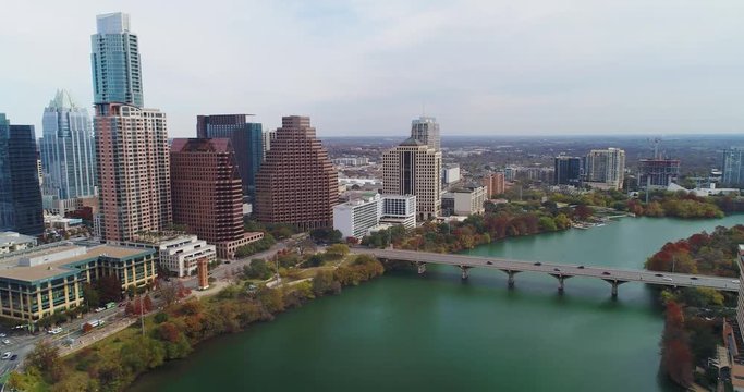 A high angle reverse aerial establishing shot of the Texas, Austin skyline with the Colorado River in the foreground. Late Autumn day with foliage trees.  	