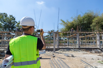 Engineers wear a helmet and holding construction plan and camera monitoring the construction area.
