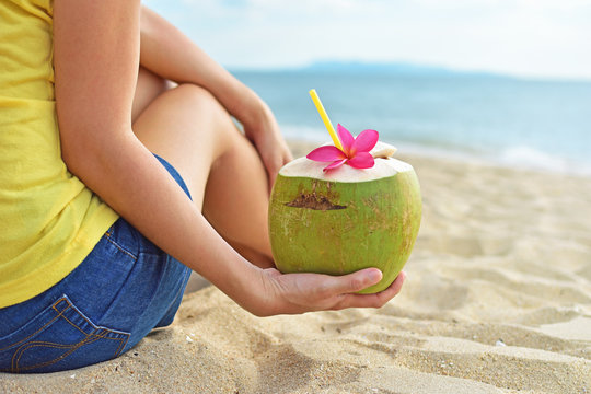 Young woman drinking fresh coconut water and sitting on the beach.