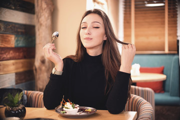 Beautiful sensual woman with dark chocolate hair eating brownie cake dessert in cafe with great pleasure