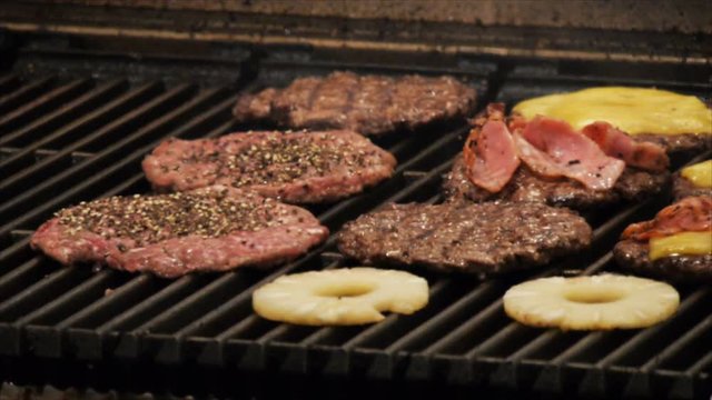 hamburger patties, pineapple and bacon cook on the grill of a restaurant