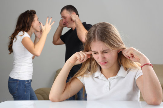 girl teenager closes ears in the background screaming at each other parents.