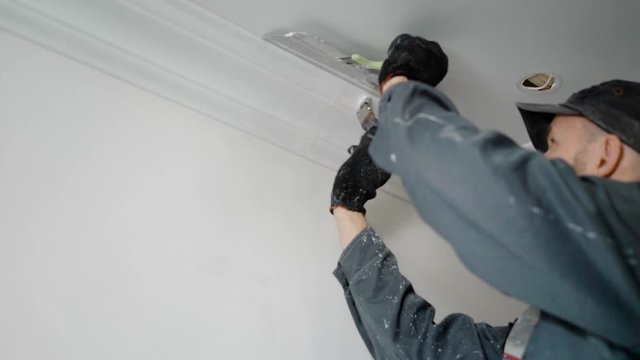 worker is painting ceiling moldings in a white color using paint brush and spatula for protection of suspended ceiling