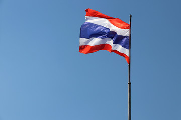 Thai national flag in blue white and red color on the flagstaff blowing with the wind on blue sky background. National flag of Thailand, three color on the fabric.