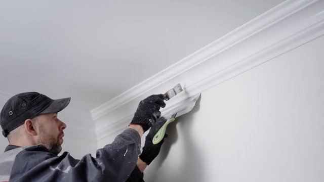 experienced painter is coloring plinth, fixing between ceiling and walls in a white, manual labor in a repair