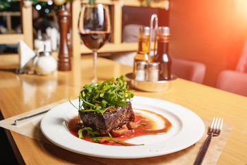 Beef steak with arugula and champignons on a white plate on the table in the restaurant. A glass of red wine, a salt, a pepper.