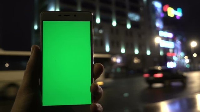 Man hand holding the white smartphone on night city light bokeh background. Green screen.
